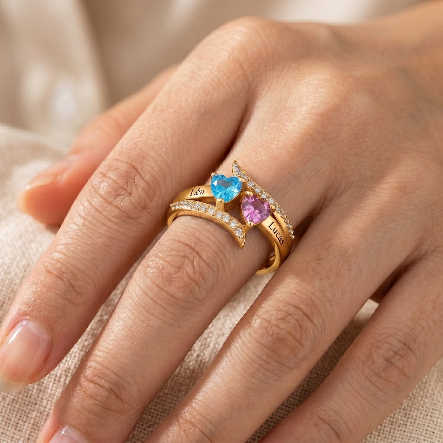 Bague cœur personnalisée portée, finition or, prénoms Léa et Lucas, pierres cœur bleue et rose